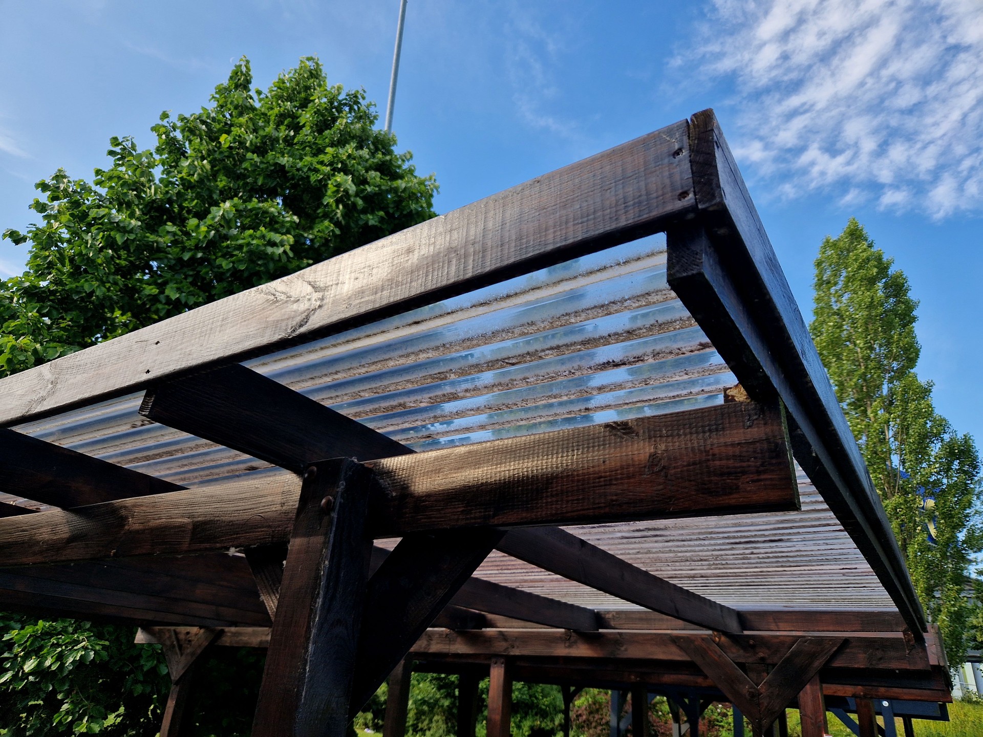terrace with wooden pergola and plexiglass roof. vines are straining, crawling under the beams. garden or park. sitting with dry wall wine region. restaurant countryside france