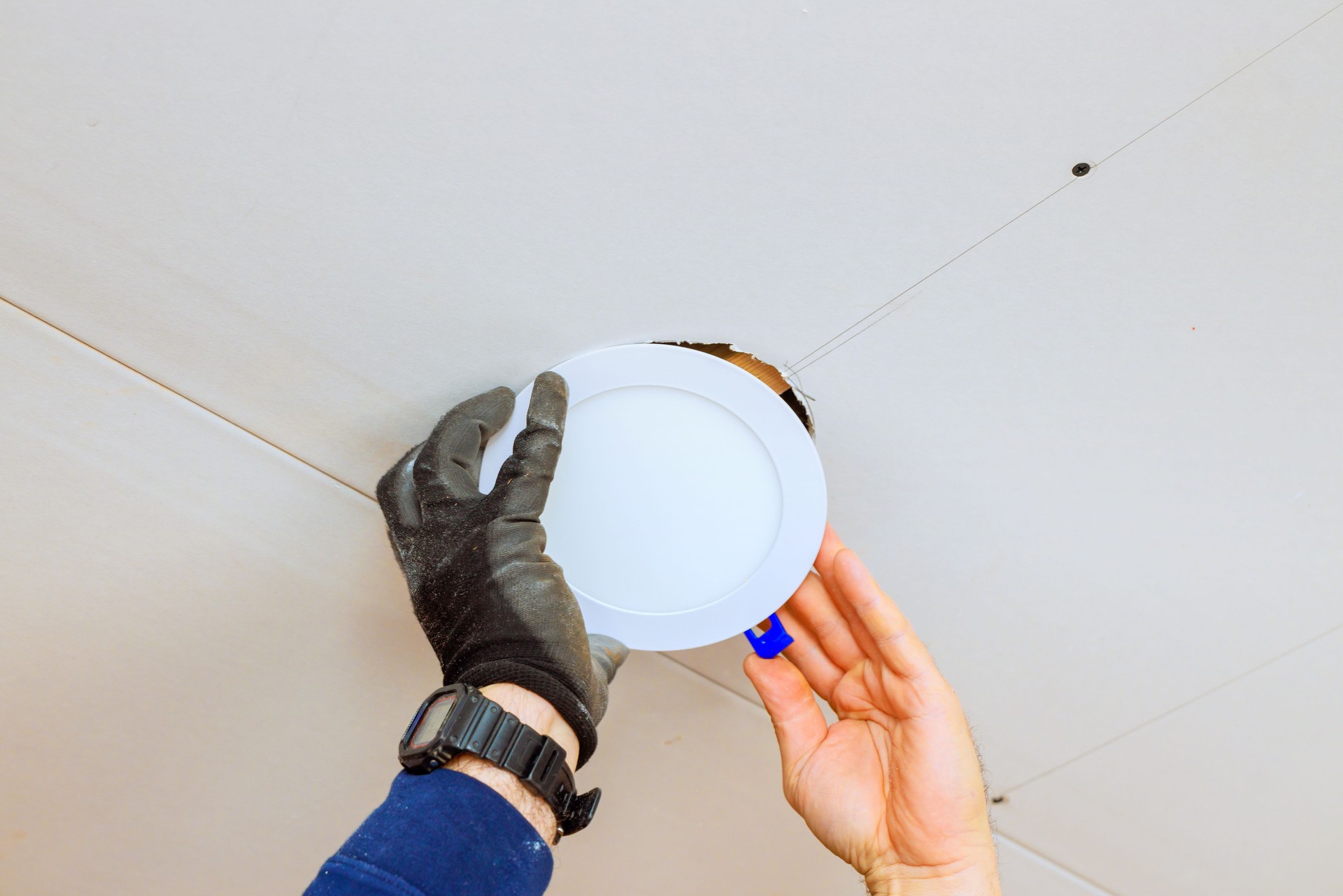 Worker installs a recessed light fixture in a ceiling during a home renovation project in daylight